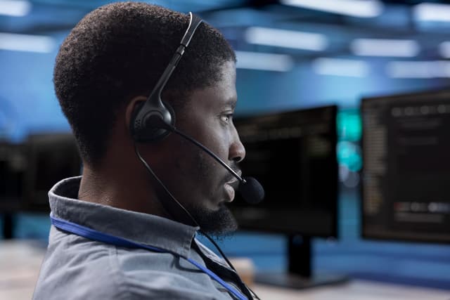 A focused operations specialist wearing a headset at a monitoring station, representing the lawful intercept operations and law enforcement liaison a CALEA trusted third party handles for carriers.